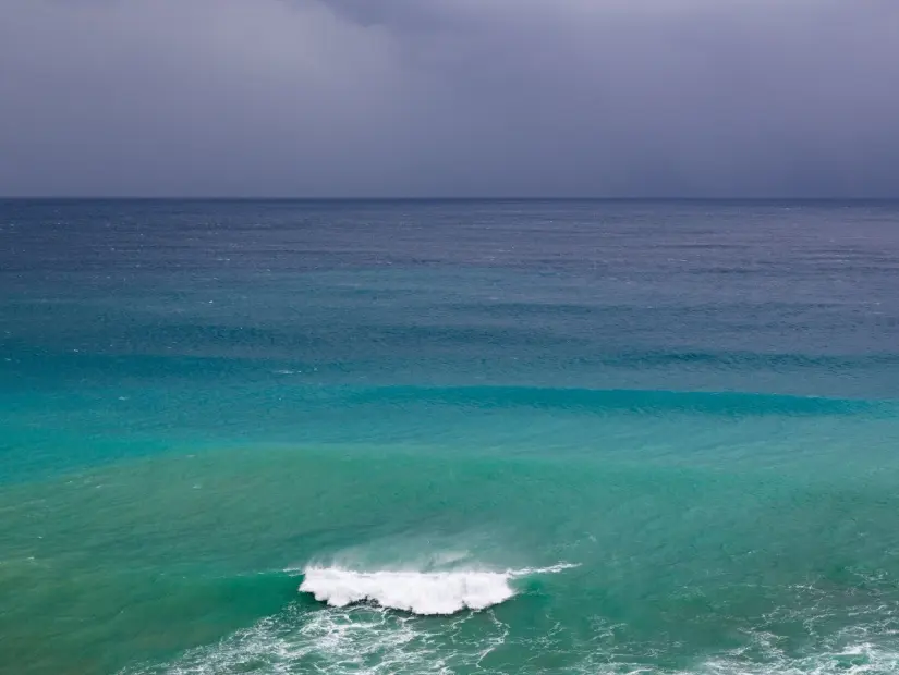 Akdeniz'in etkileyici arka plan fotoğrafı. Denizin yeşil, turkuaz, mavi, lacivert renkleri yağmur bulutlarının gri rengiyle birleşiyor. Bu güzel manzaraya küçük dalgalar eşlik ediyor.