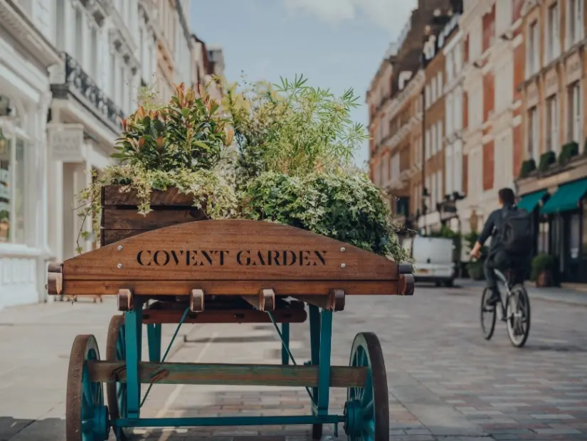 Covent Garden, Londra, İngiltere'de bir sokakta çiçeklerle dolu ahşap bir arabanın üzerinde 'Covent Garden' alan adı tabelası