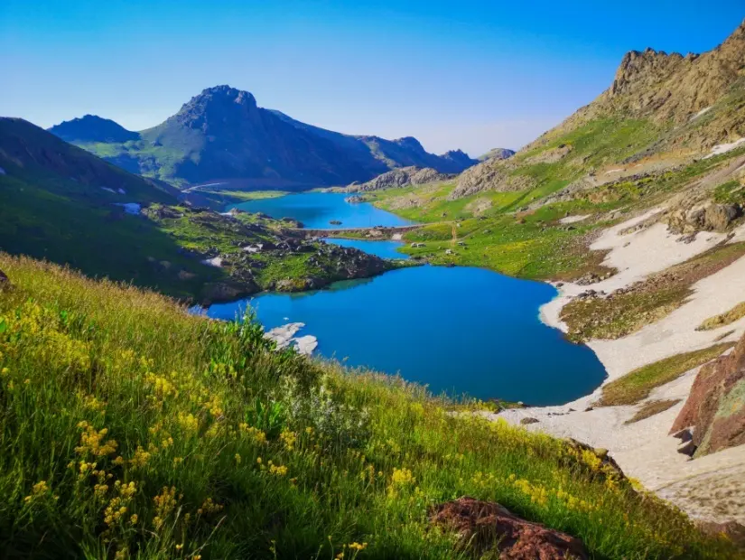 Dağlarda bir göl, doğal manzara, yeşil çayırlar, karlı dağlar, mavi gökyüzü, kış sezonu. 
