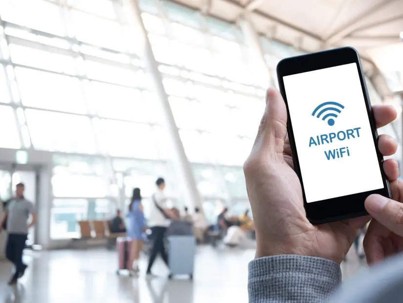 Havaalanına ücretsiz Wi-Fi bağlayan mobil akıllı cep telefonu kullanan adam, arka planda bagajla yürüyen yolcu, 